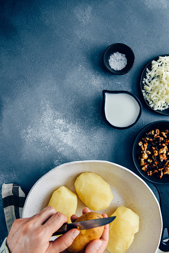 Hands peeling cooked potatoes with a knife in a white ceramic bowl