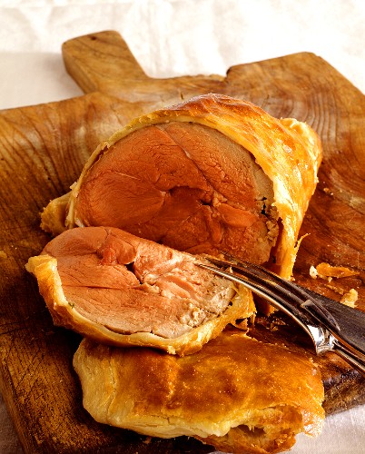 Boned leg of lamb in puff pastry on wooden chopping board