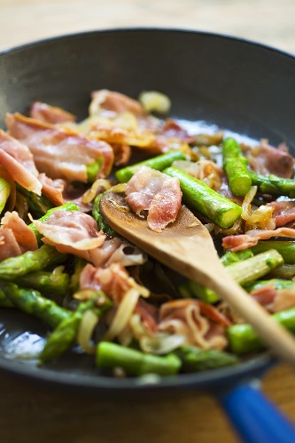 Sweating green asparagus and prosciutto in frying pan 