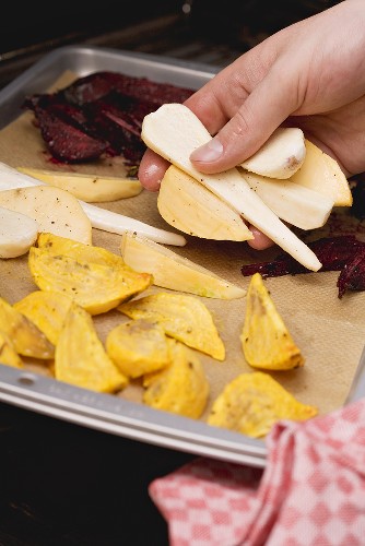 Sliced vegetables being placed on a baking tray