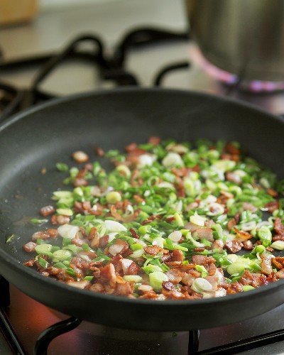 Frying peas with spring onions and bacon in a frying pan
