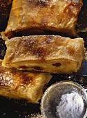 Viennese apple strudel on baking tray; a piece cut