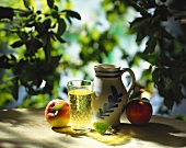 Apfelweinstilleben mit Steingutkrug auf einem Gartentisch