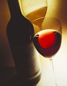 Stillleben mit Rotweinglas vor etikettierter Rotweinflasche