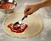 Spreading tomato sauce on pizza