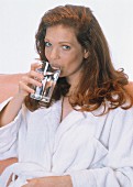Rothaarige Frau im Bademantel trinkt ein Glas Wasser