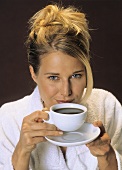 Blonde Frau im Bademantel hält Kaffeetasse in den Händen