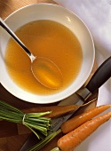 Clear Chicken Broth in Bowl with Spoon and fresh Carrots
