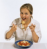 Model eating spaghetti with tomato sauce from blue plate