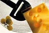 Ein Stück Emmentaler mit Käsehobel & Weintrauben auf Teller