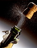 Korken springt aus dem Hals einer Champagnerflasche