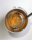 Drei aufgeschlagene rohe Eier & Schneebesen in der Schüssel