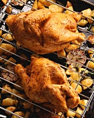 Two roast chickens on rack above baked potatoes, sweetcorn