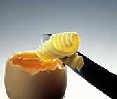 Messer mit Butter über einem aufgeschlagenen gekochten Ei