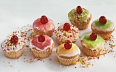 Several muffins with coloured icing and sprinkles