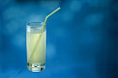 Zitronenlimonade im Glas mit Strohhalm vor blauem Hintergrund