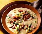 Potato cream soup with vegetables & sausage in soup plate