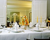 Festlich gedeckter Tisch mit Rosengesteck in Silberschale und Blick durch Flügeltür ins Wohnzimmer