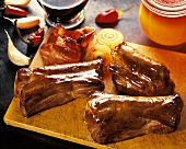 Three spare ribs on wooden board; bacon and onions