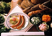 Frankfurter sausage on plate, bread, salads beside it
