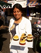 Mexican woman holding plate of sweet jelly tarts (in open air)
