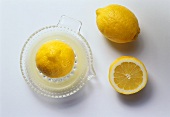 Zitronenhälfte auf Presse, daneben Zitrone und Zitronenhälfte