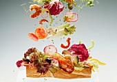 Sandwichzutaten (Salat, Gemüse etc.) fallen auf Baguettestück