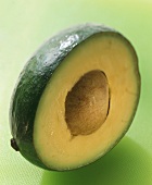 Half an avocado with stone on light-green background
