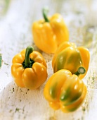 Four yellow peppers on white wooden background
