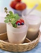Berry milk shake in glasses on tray, spoon with berries above
