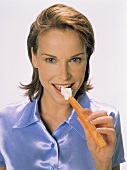Young woman eating carrot with cream cheese dip