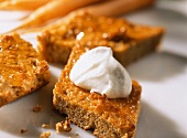 A few pieces of carrot cake, one with a blob of whipped cream