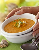 Hands holding a bowl of carrot soup