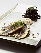 Spicy marinated sardines, behind black ribbon noodles