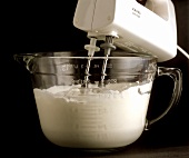 Whipping cream with a mixer against a black backdrop