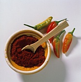 Paprika with wooden spoon in small bowl, red pepper beside it