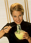 Blond woman eating Asian noodle soup with chopsticks