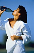 Junge Frau im Bademantel trinkt Wasser aus einer Flasche