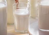 A glass of milk surrounded by milk bottles