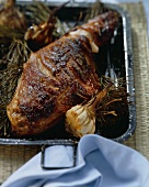 Leg of suckling pig with garlic & fir sprigs in a roasting tin