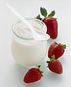 Jar of natural yoghurt & spoon, fresh strawberries beside it