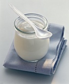 A jar of yoghurt with spoon on pale blue cloth