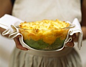 Woman holding glass dish of baked layered puree