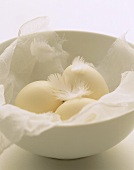 Three eggs with feathers in a bowl