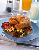 Croissant topped with scrambled egg, bacon & tomato