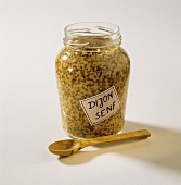 Granular Dijon mustard in jar, wooden spoon in front