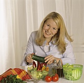 Junge Frau schneidet Gurke in gemischten Salat