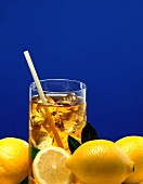 A glass of iced tea with ice cubes & straw, lemons in front