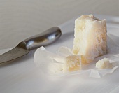 A piece of parmesan with knife on a chopping board