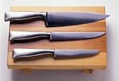Drei hochwertige, geschmiedete Messer auf einem Holzbrett